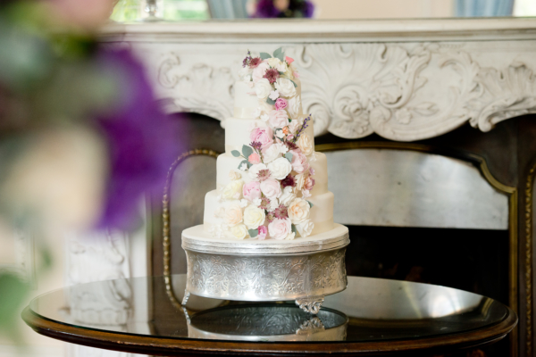 A white, tiered wedding cake with a cascade of pastel flowers down the front.