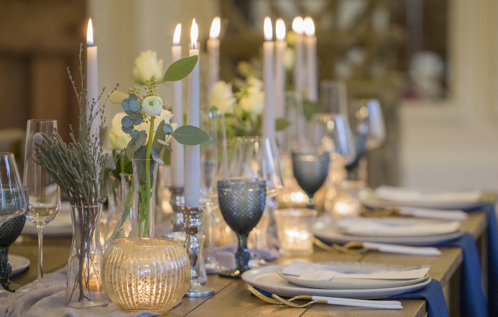 Close up of a table set up, blue glasses, muted flowers and lit candles