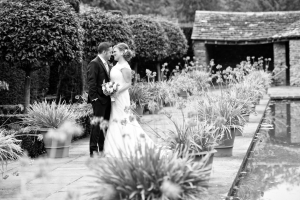 A black and white photo of a bride and groom with pots of flowers stretching alongside them.