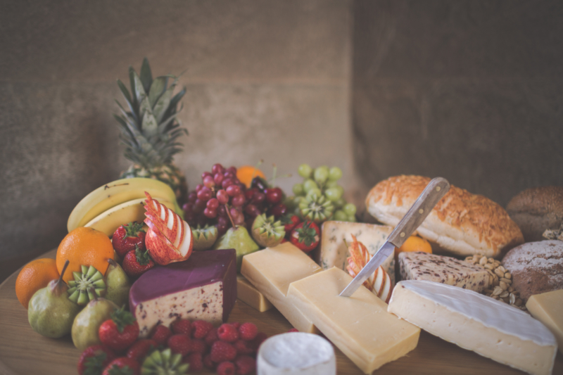 A cheese board piled up with fruit, cheese and bread.