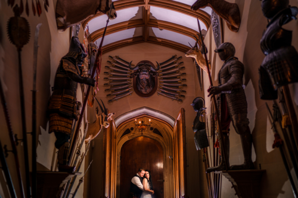 Wedding couple standing in doorway at end of ornate corridor with armour and swords