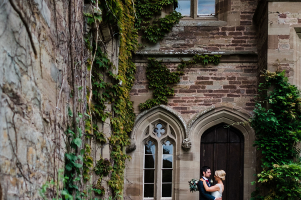 Couple standing on steps under castle wall and vines