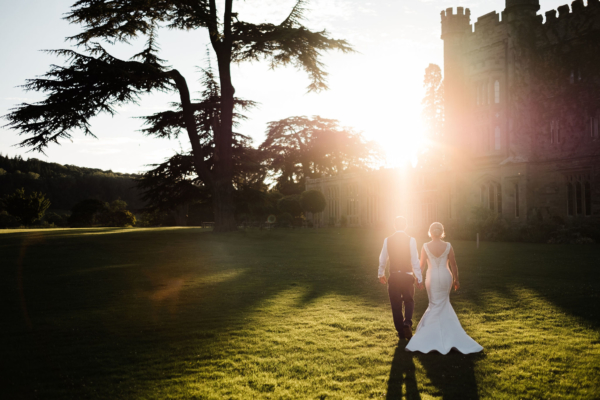 Wedding couple waling hand in hand across lawn in sunshine
