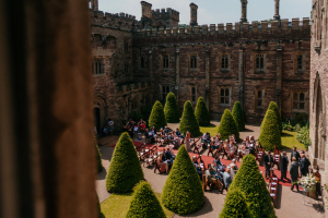 People sitting on benches in a castle courtyard, waiting for a wedding to start