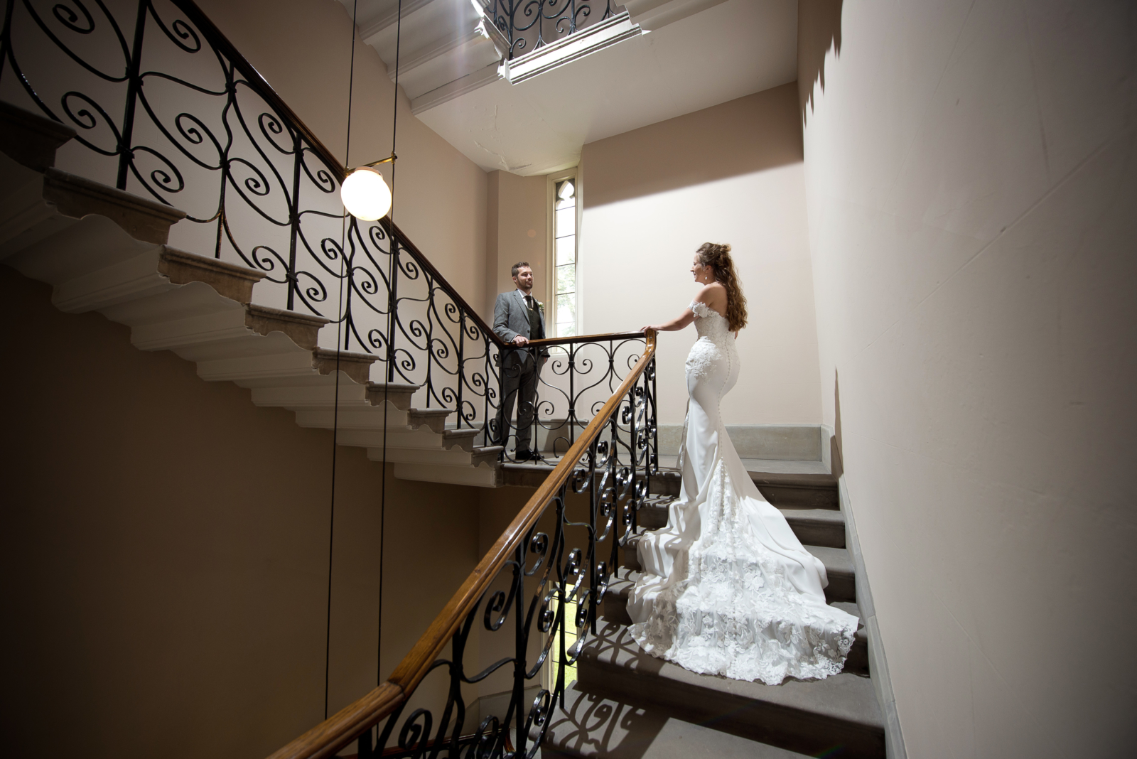 A bride and groom gaze at each other on the landing of a cantilevered staircase