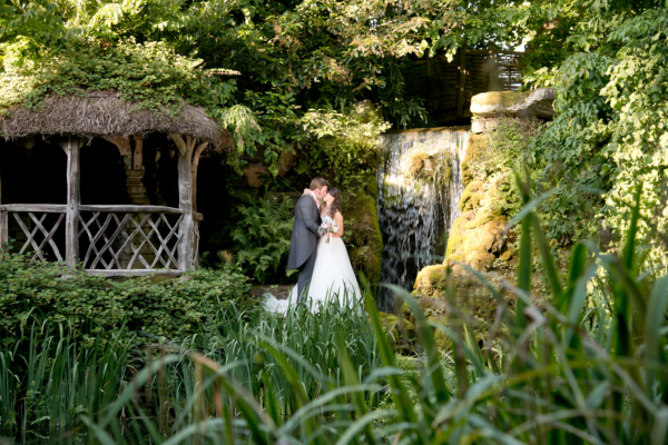 Couple kissing with shelter to left and waterfall to right in green garden.