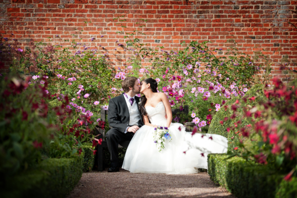 Couple kissing on bench surrounded by cosmos and nicotiana flowers