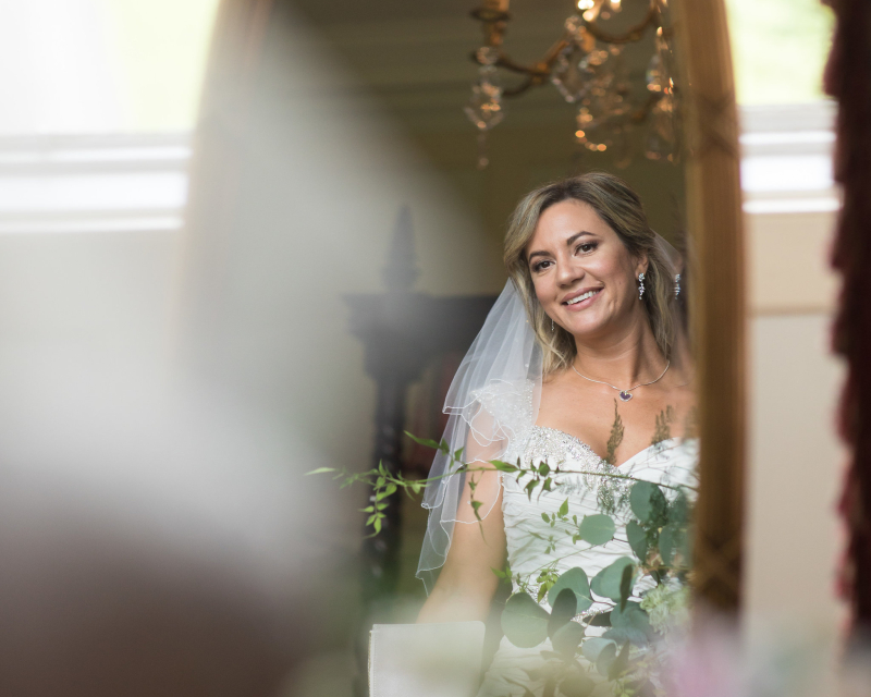 Bride's reflection in mirror with chandelier and flowers