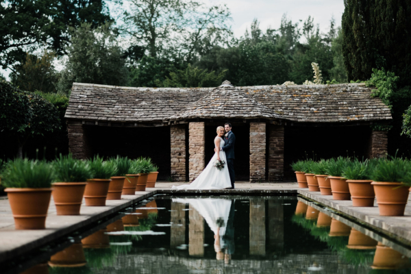 Wedding couple in front of hut with canal in foreground.