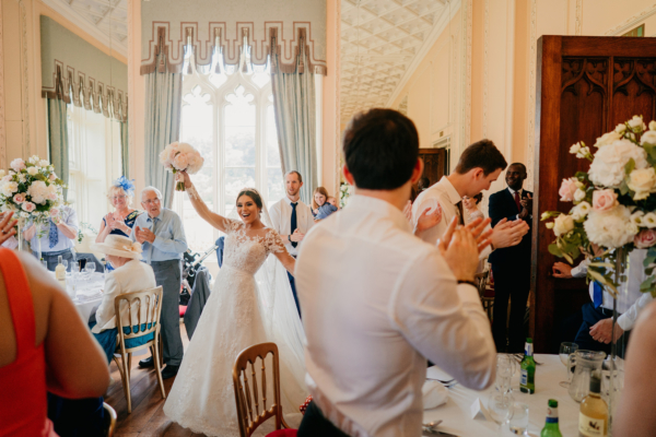 Bride raising bouquet in celebration surrounded by guests in ballroom