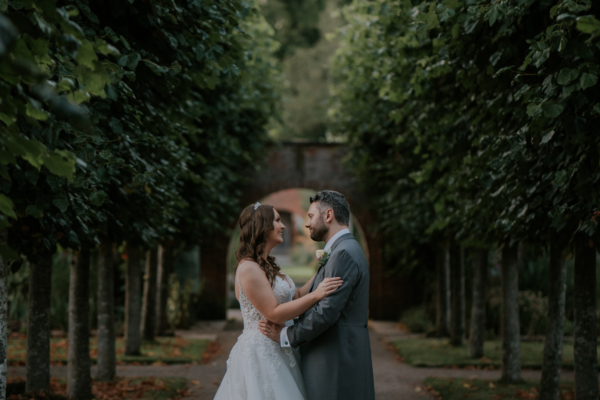 Wedding couple facing each other in walkway of gardens