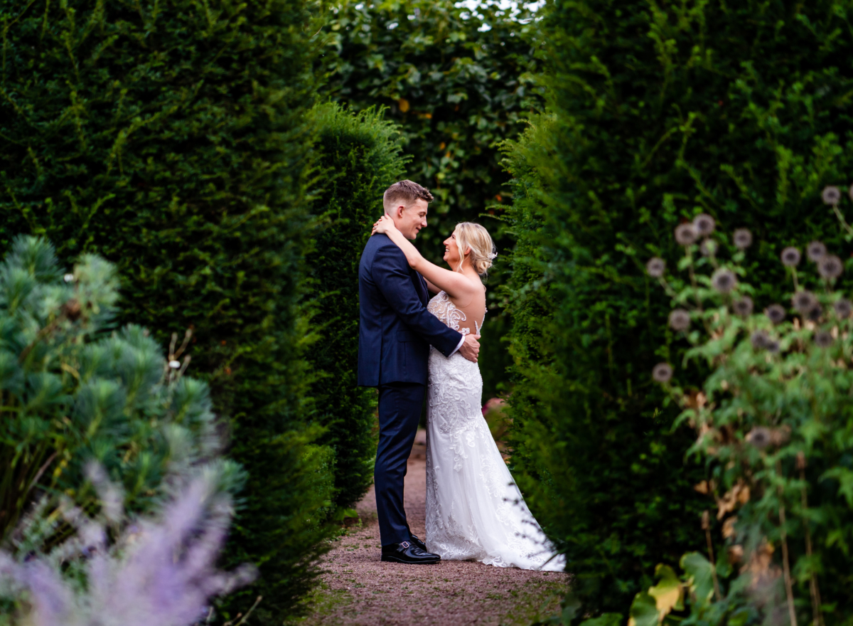 Couple stand between hedgerows for photo