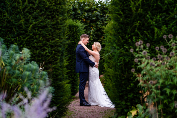 Couple stand between hedgerows for photo