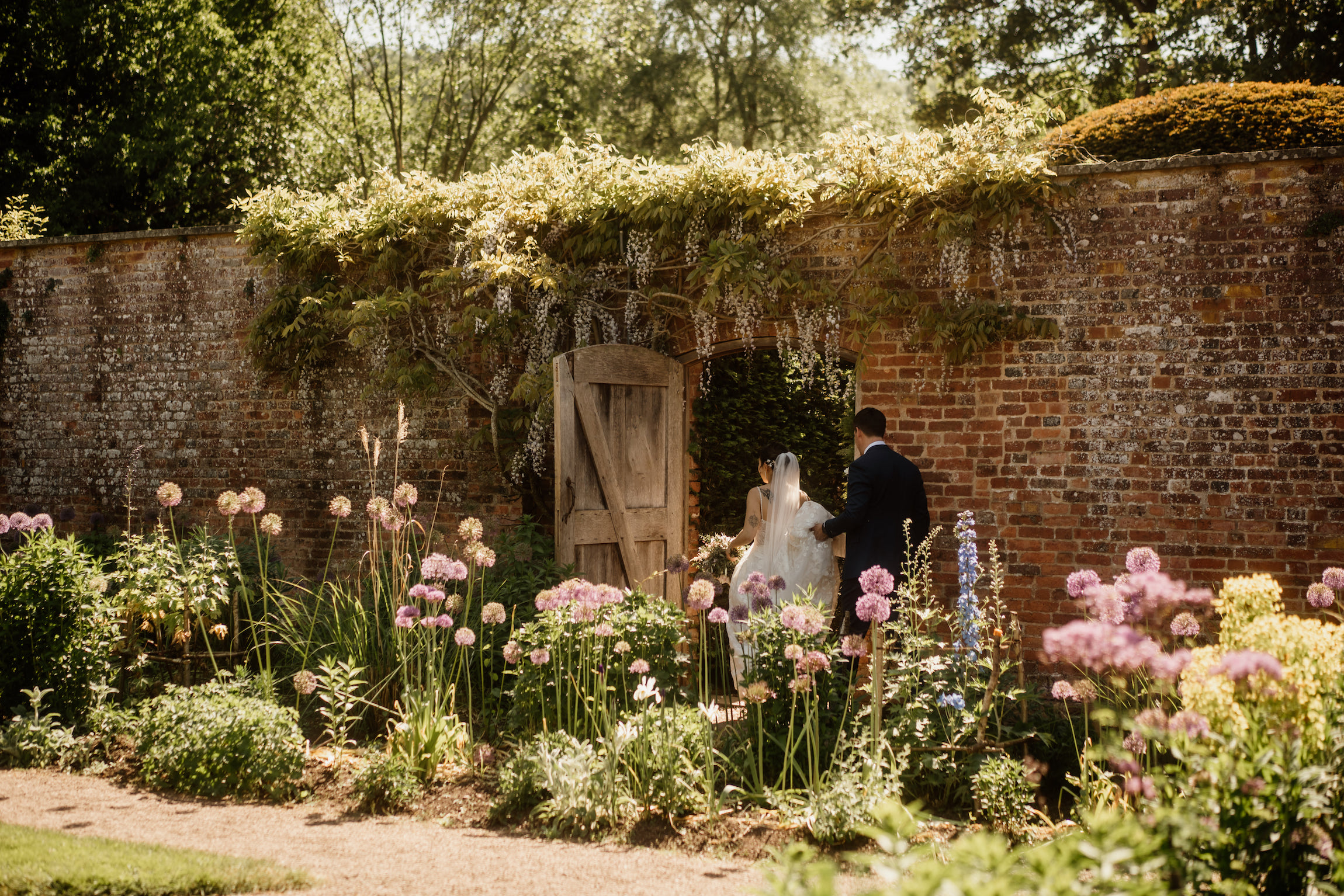 Couple walking through walled rose garden at Hampton Court Castle wedding venue